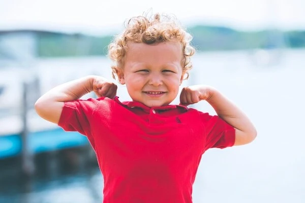 Curly-haired child in red shirt showing strength